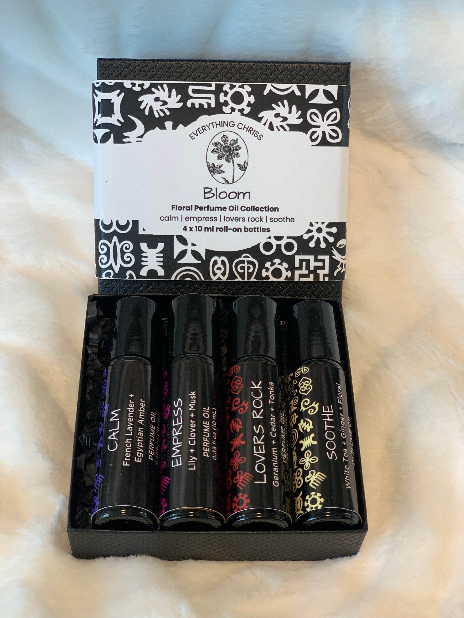 Set of black perfume oils with visible brand names in a box on a textured white surface